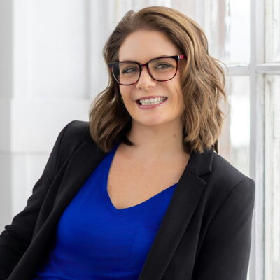 Smiling woman in blue shirt and blazer, sitting by window.