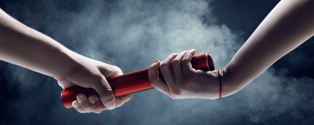 Hands passing a red baton in a smoky atmosphere, symbolizing teamwork and connection.