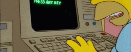 A humorous scene from "The Simpsons" showing Homer Simpson sitting at an old computer. The screen displays the text "TO START PRESS ANY KEY," and Homer says, "Where's the 'any' key?" The image highlights a classic comedic moment about technology confusion